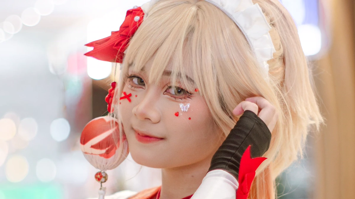Convention cosplayer with a blonde wig, soft blush and small red face details Cosplayer at an indoor convention with a blonde wig and maid headband, soft blush, red dots and a small cross drawn on the cheek