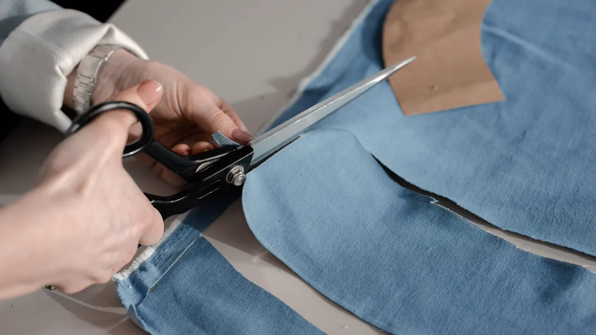 Hands cutting a thrifted denim piece with tailor scissors on a work table Hands cutting a pair of thrifted blue jeans with black tailor scissors, the kind of first alteration a beginner cosplay costume needs