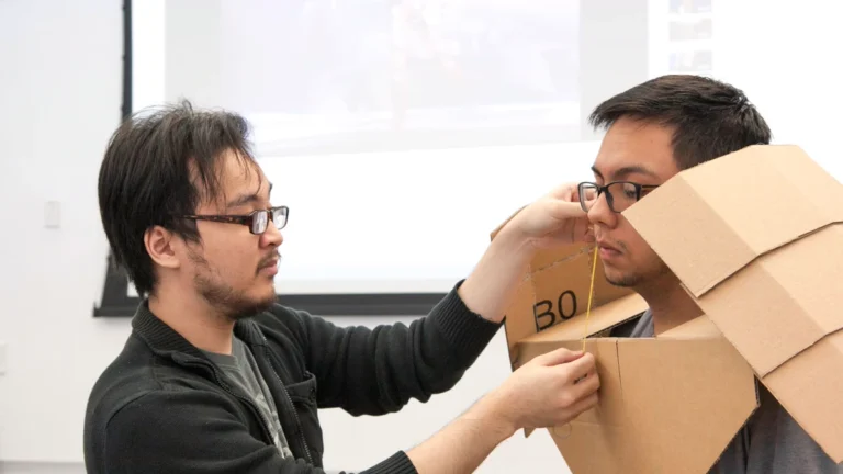 Cardboard Armor: 4 Pieces From Free Boxes vs EVA Foam 1 Cardboard armor fitting: one student measures a classmate wearing a chest and shoulder piece folded from a brown shipping box