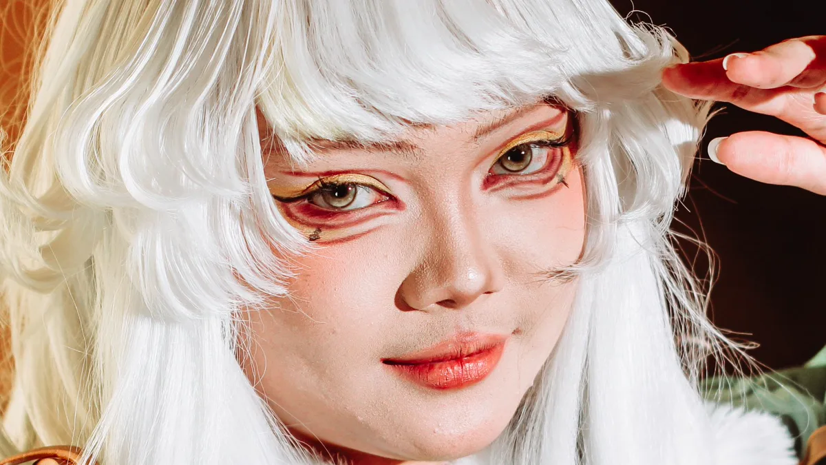 Cosplayer in a white wig with graphic red and gold eye makeup Cosplay makeup close-up: a cosplayer in a white wig with red graphic liner under the eyes, gold shadow and a red lip