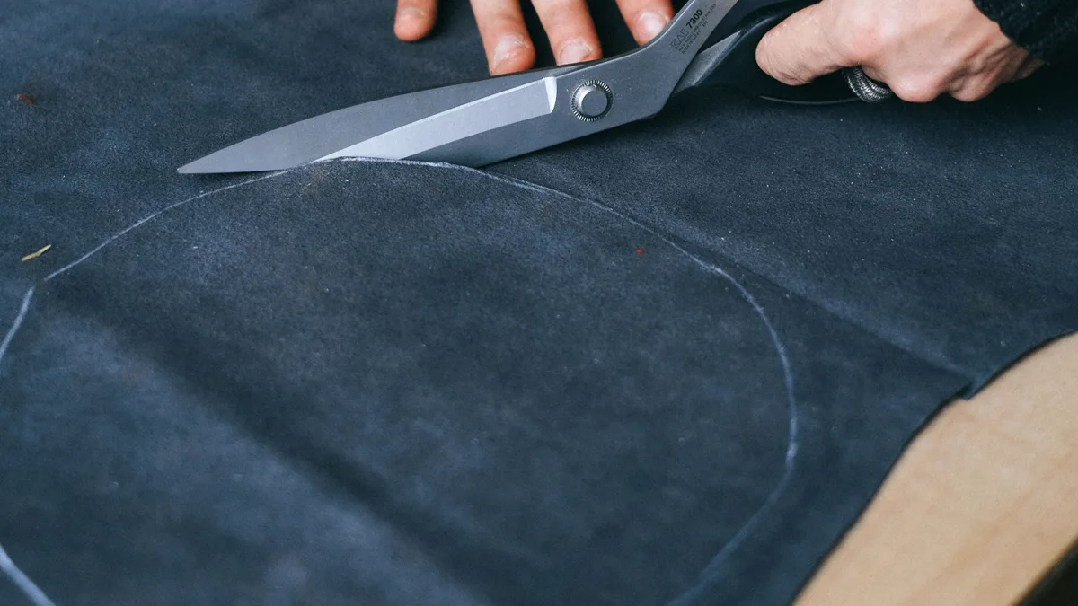 Hands cutting along a chalk curve on dark fabric with large tailor shears Large shears following a chalk-drawn curve on dark fabric, the same string-and-chalk circle used for a no-sew cape pattern