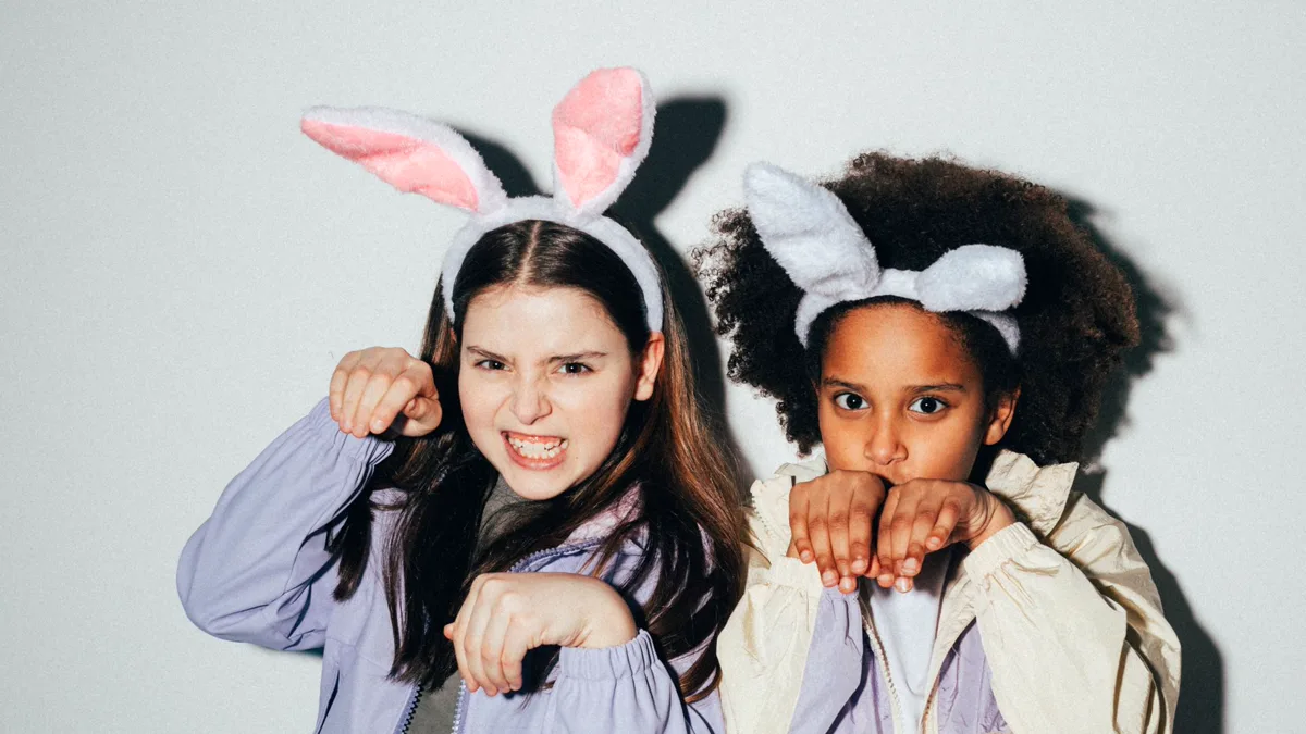 Two girls in duo Halloween costumes made from bunny ear headbands and everyday jackets, posing with paws raised