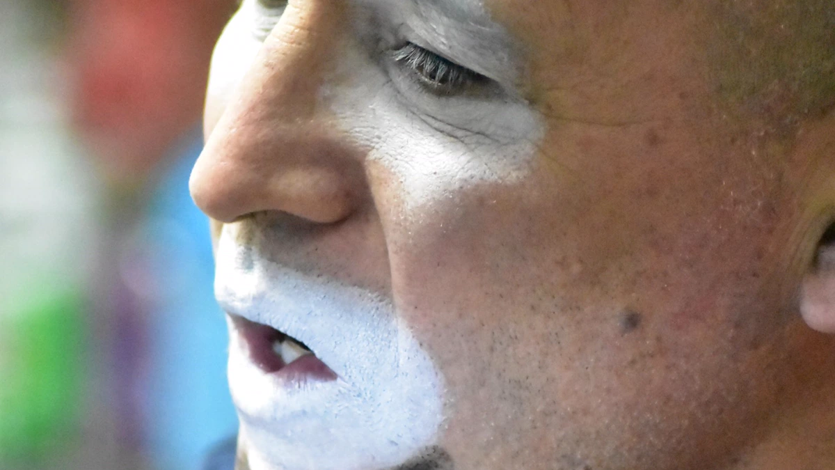 Man blending white clown makeup base around his mouth and under his eye with a fingertip, close up side view