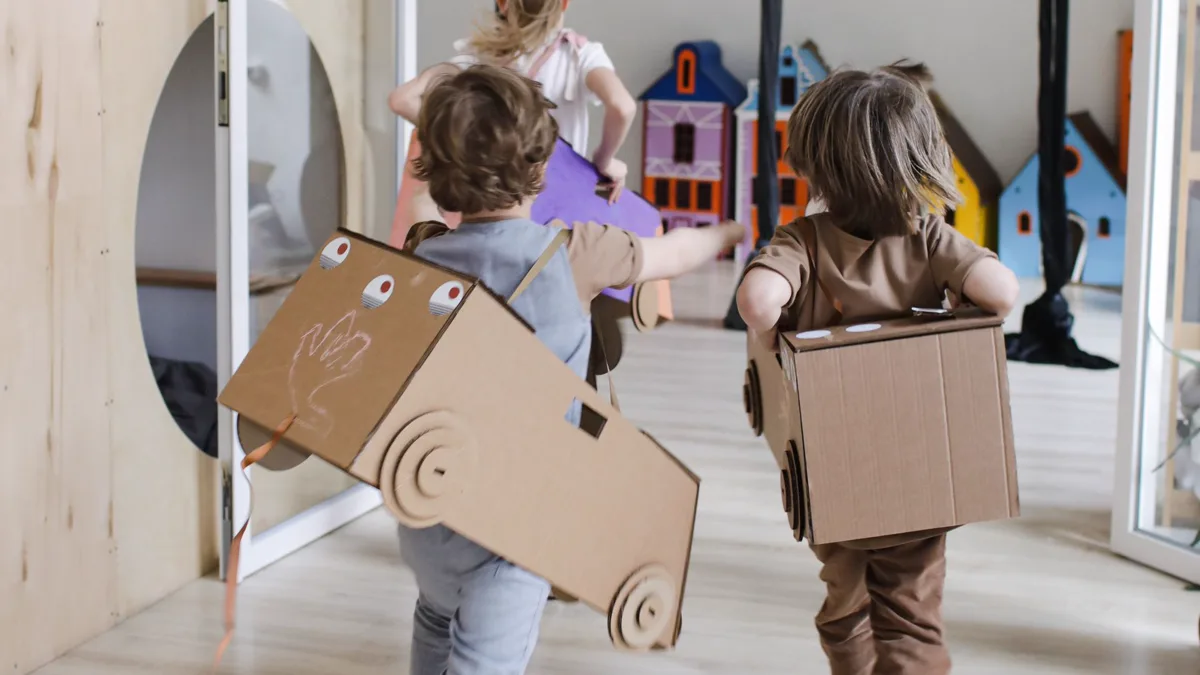 Two kids running down a hallway in easy duo costumes built from cardboard boxes with cardboard wheels