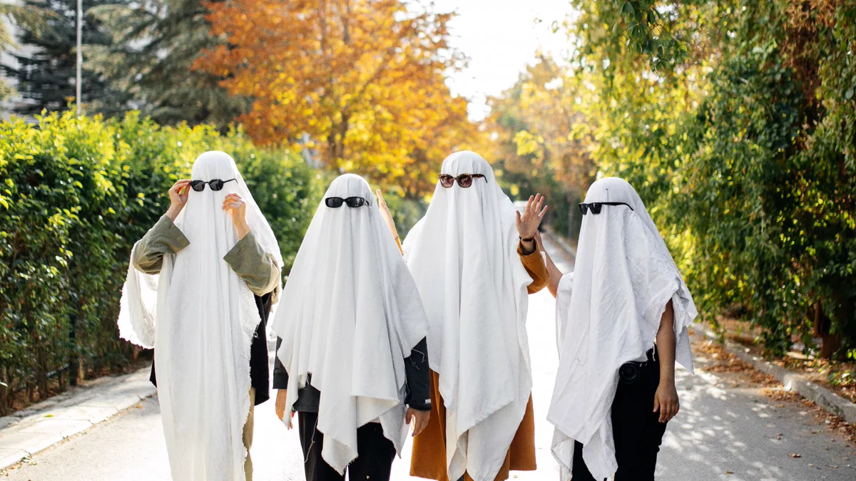 Four people in white sheet ghost costumes with black sunglasses walking down a leafy road, a free group costume idea for four