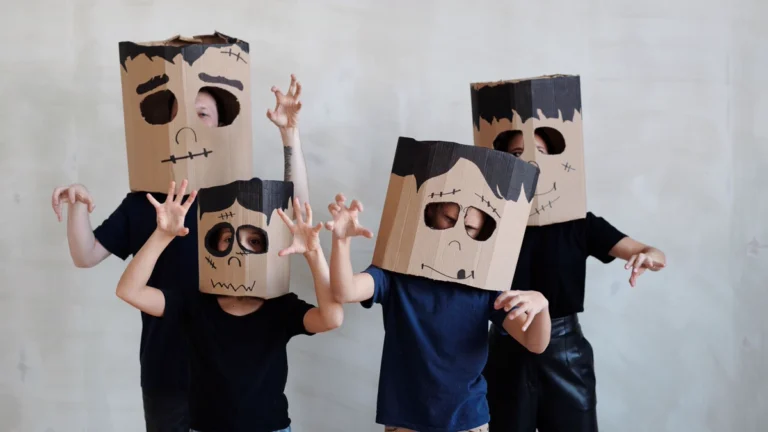 Four friends in DIY group Halloween costumes made from cardboard boxes painted as monster heads with black hair and stitched mouths