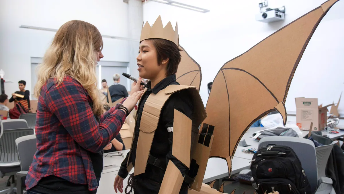 Student in a homemade cardboard dragon costume with large bat-shaped wings, armor plates and a cardboard crown