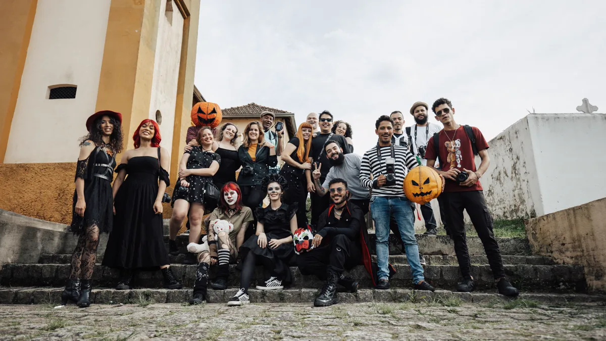 About twenty friends in witch hats, black dresses and painted faces holding jack o'lanterns on outdoor stone steps
