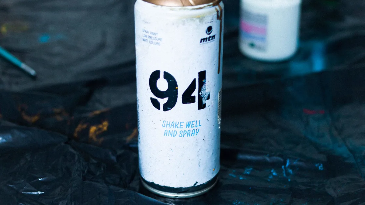 A white spray can standing on a black plastic drop cloth beside a jar of paint, ready for sealing and painting cosplay armor outdoors