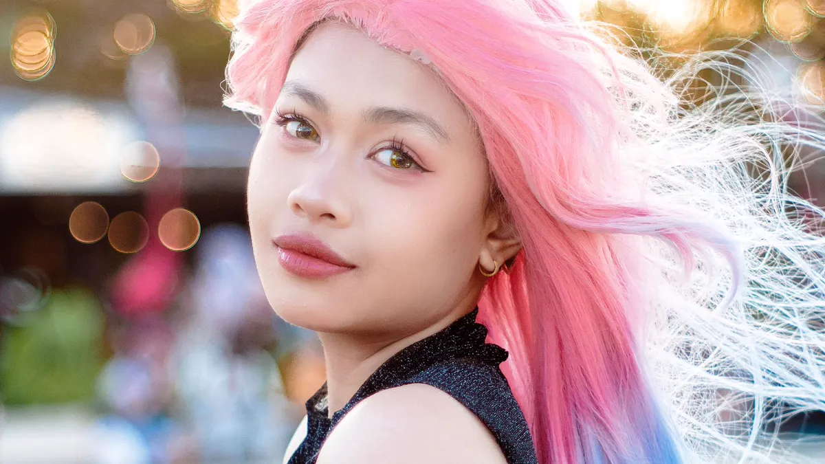 Long pink to blue ombre wig worn outdoors at a fan event Secure cosplay wig fit: a long pink to blue ombre synthetic wig worn outdoors, fibers lifting in the breeze at a fan event