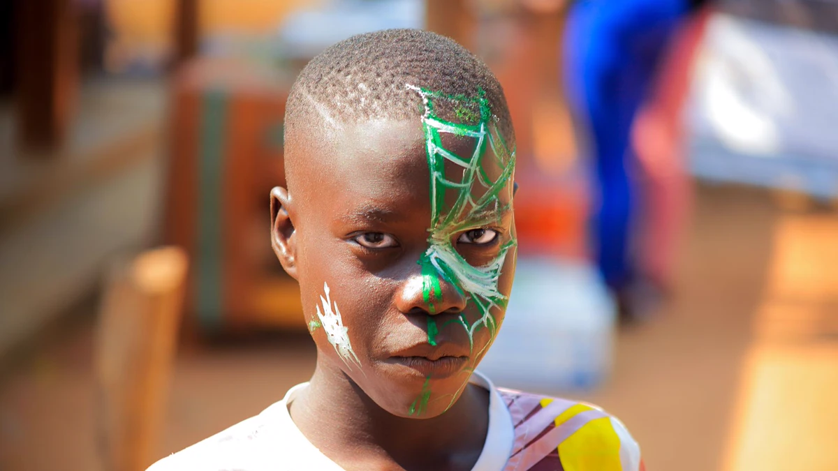 Boy with a green and white spider web painted on half his face Boy with a green and white spider web face paint covering one side of his forehead and cheek, outdoors at a market