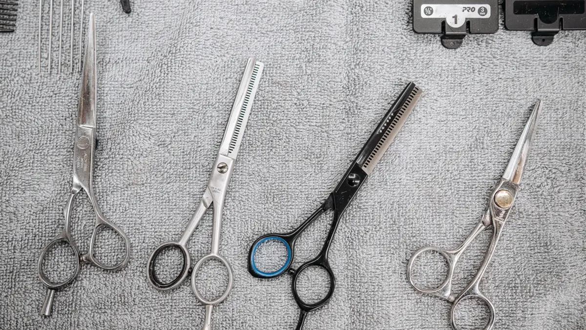 Straight hair shears and thinning shears laid out on a grey towel Wig bang cutting tools: two straight hair shears and two thinning shears laid side by side on a grey towel next to clipper guards